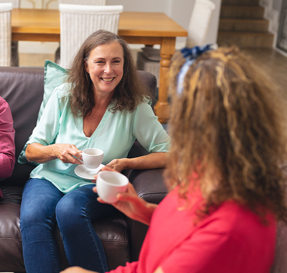two women enjoying tea on a couch the scene captures a cozy moment with friendly conversation and laughter while the background shows a tastefully decorated living space perfect for relaxation and socializing with friends discussing plans for a gathering or celebration with seven important friends